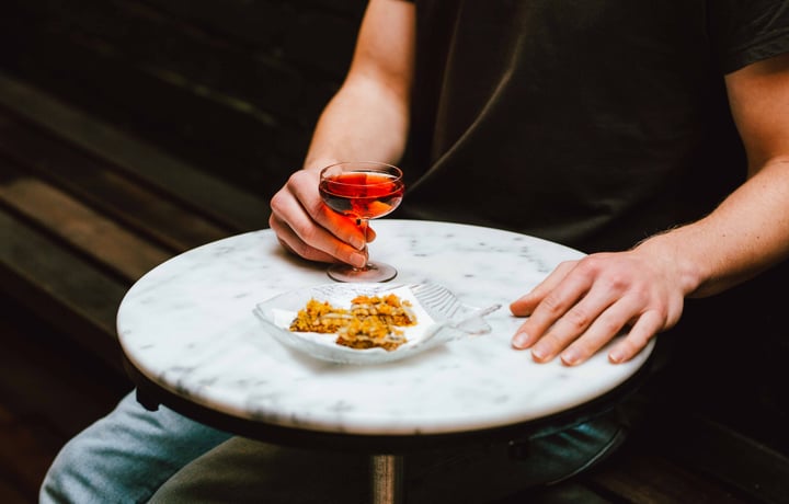A hand holding a glass of rose next to a plate of food.