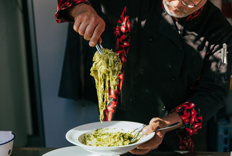 A chef serving a plate of spinach pasta on a plate in the sunlight.