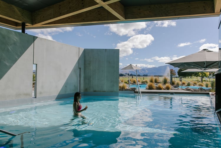 A woman walking through the water at Opuke Thermal pools with the Southern Alps in the background.