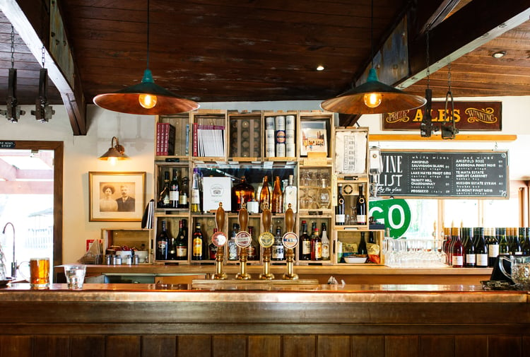 A wooden bar with green downlights where there are 4 beers on tap.