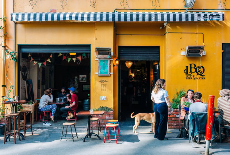People dining outside a bar that has a yellow painted exterior.