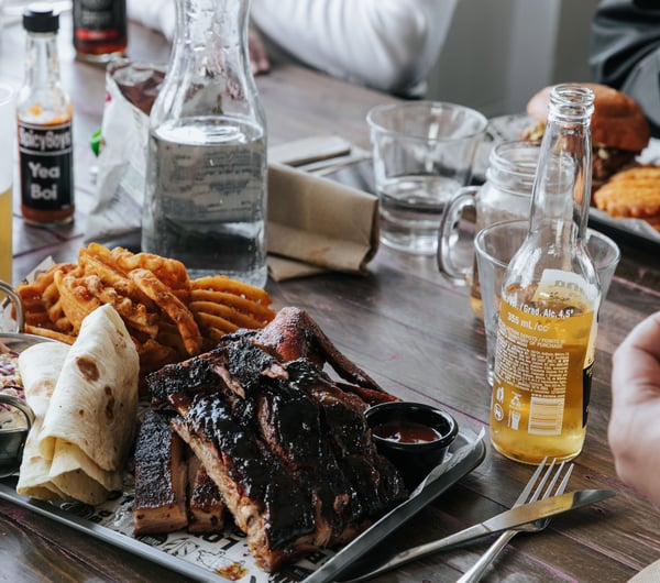 A plate of meat and chips on a table sittling alongside beers.