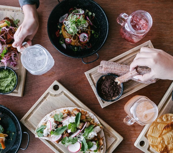 Hands reaching for different types of Mexican food on a table.e