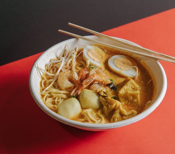 A plate of laksa on an orange table.