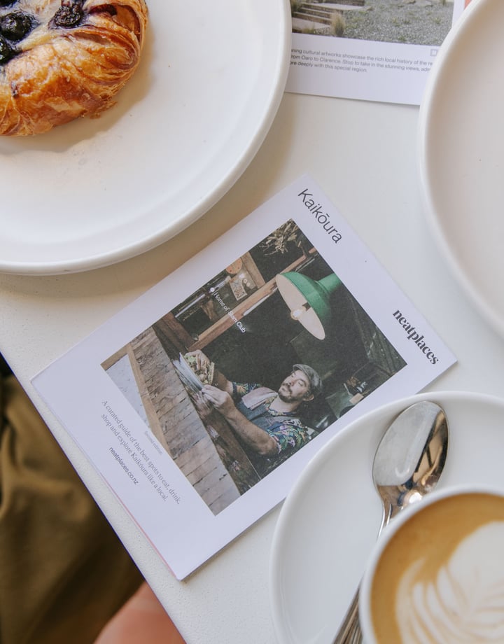 A photo of the latest Kaikoura pocket guide sitting on a table next to coffee and pastries.