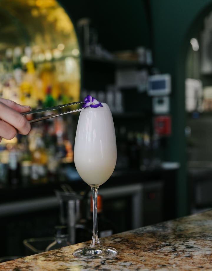 Bartender adding purple pansy as a garnish on top of a cocktail