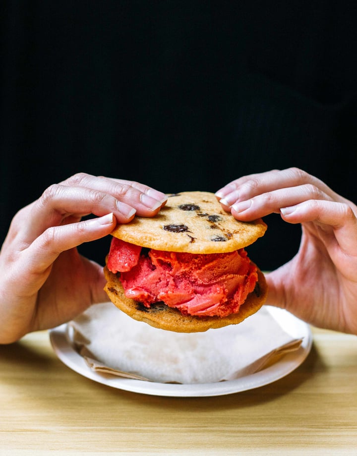 Two hands holding an ice cream cookie sandwich.