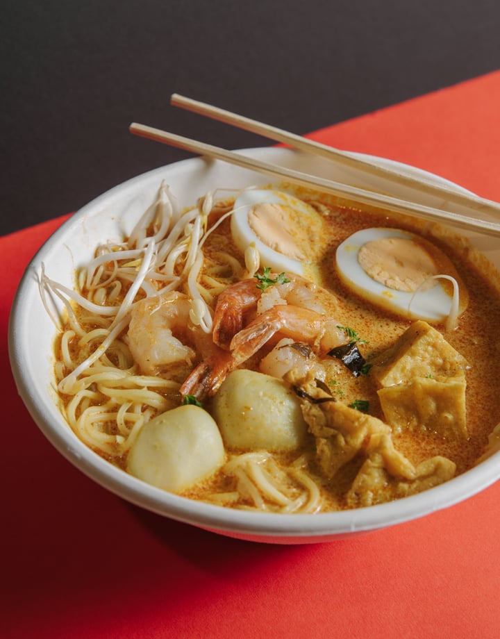 A plate of laksa on an orange table.