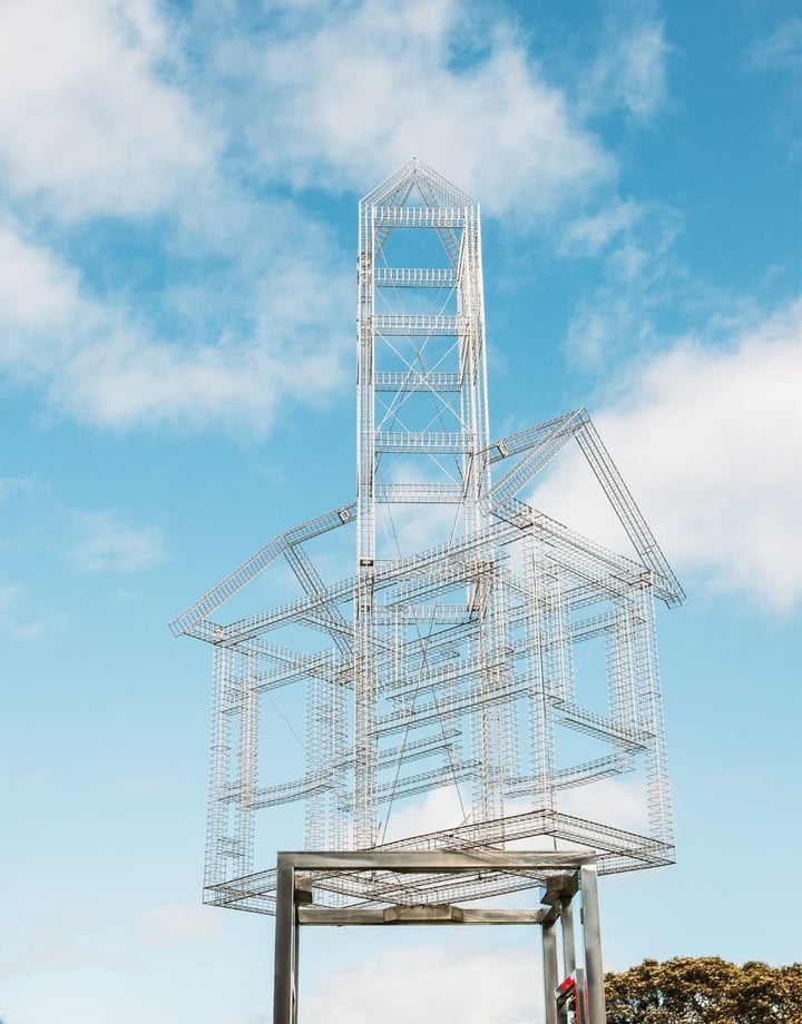 A sliver metal sculpture of a house frame on stilts.