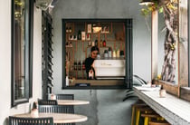 A barista working behind a small hole-in-the-wall window.