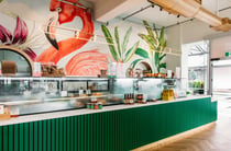The green counter inside Long Island Delicatessen with a backdrop of a flamingo painted on the wall.