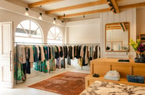 Interior of boutique clothing store with rows of clothing next to big arched windows