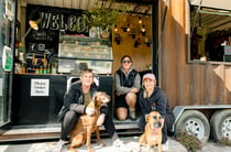 The three team members behind Red Bridge Coffee sitting outside coffee trailer with their two dogs