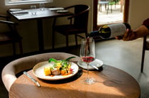Waiter pouring glass of red wine next to a refined plate of food