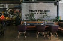 An indoor seating area with 'Two Thumb' printed on a brick wall.