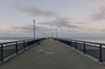 A couple walking along New Brighton pier in the evening with pinky skies and calm waters in the background