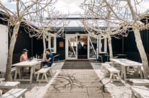 A couple dining outside a black barn on a sunny day.