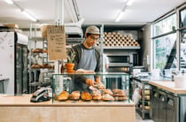 Worker behind cabinet serving almond croissant onto plate using tongs.