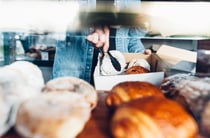 Person in denim jacket using tongs to put donuts and croissants into a take away container.