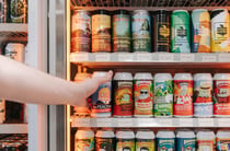 Hand reaching into fridge to grab a can of craft beer.