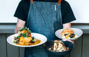 A staff member holding three plates of food at Kika in Wānaka.