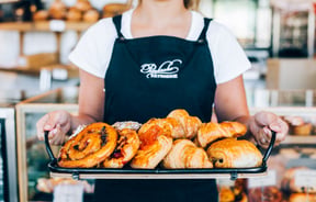 A staff member holding tray of freshly baked pastries.