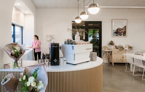 A female staff member working behind a white and timber cafe counter.