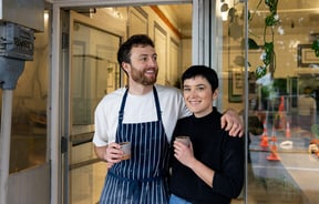 A man and woman looking at the camera outside their afe.