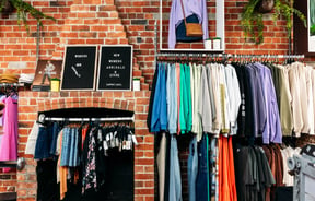 Colourful clothes up against a brick wall inside a retail store.