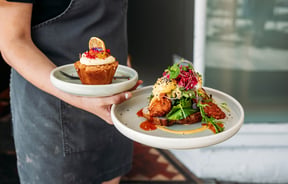 Close up of waitstaff holding a savoury brunch plate and a cake on another plate.