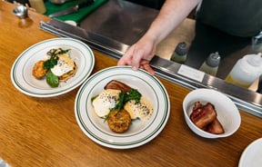 An outstretched arm places a plate of bacon and eggs and hollandaise on the pass at Cream Eatery in Hamilton.