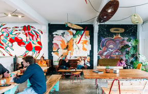 People enjoying coffee on the vintage couches with artwork behind them at Escape Coffee Roasters, New Plymouth.