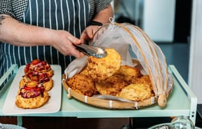 Waiter picking up a cheese scone from under mesh cloche with tongs