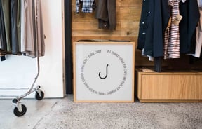 Black and white fishing hook sign on floor by clothing racks.