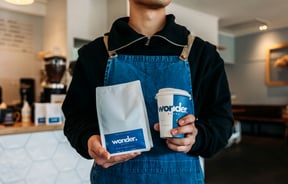 Close up of a staff member in an apron holding a bag of Grey Roasting Co. coffee beans.