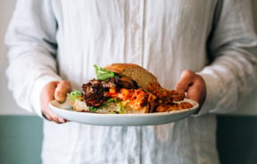 Two hands hold a plate with a colourful sandwich on it at Hayes Common, Hamilton.