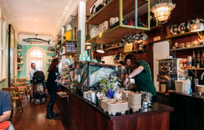 Barista making coffee behind cafe counter and cabinet
