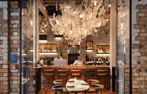 A staff member working behind at the bar inside a lush restaurant.