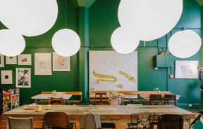 Large tables with low hanging lights set against dark green walls.