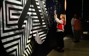 Woman looking at an exhibition and taking a photo of it at Pātaka Art + Museum.