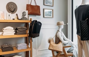 Folded knitwear on wooden shelves and mannequins accessorised with hats and woven shoulder bags.