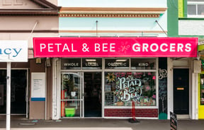 Shop exterior with bright pink signage for Petal & Bee Grocers.