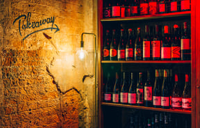 Shelves of wine with a takeaway sign.