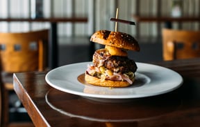A close up of a giant, tall burger on a table.