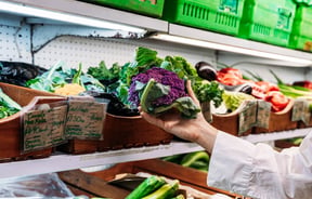 A full shelf of green vegetables in wooden boxes.