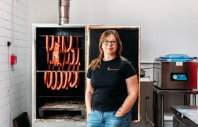 Portrait of Anna next to hanging sausages at The Polish Sausage Company in Lyall Bay Wellington