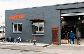 Warehouse building exterior with roller doors open and customers walking in to The Roastery.