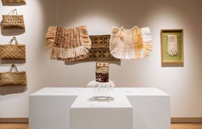 Weaved bags and mats on display inside a gallery.