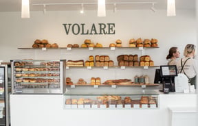Front counter of Volare Bread with cabinet and shelves filled with bread and pastries.