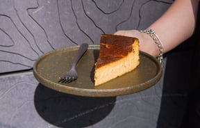 A hand holding a slice of cheese cake on a plate.